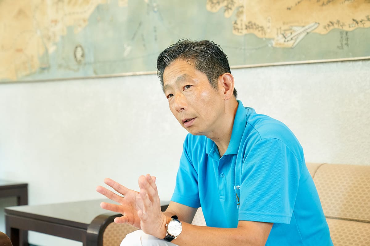 ホテル白菊代表取締役社長の西田陽一さん。お話を伺った本館1階ラウンジ「つる」の背後には、開業当初からあるという大分県の大きな地図も。